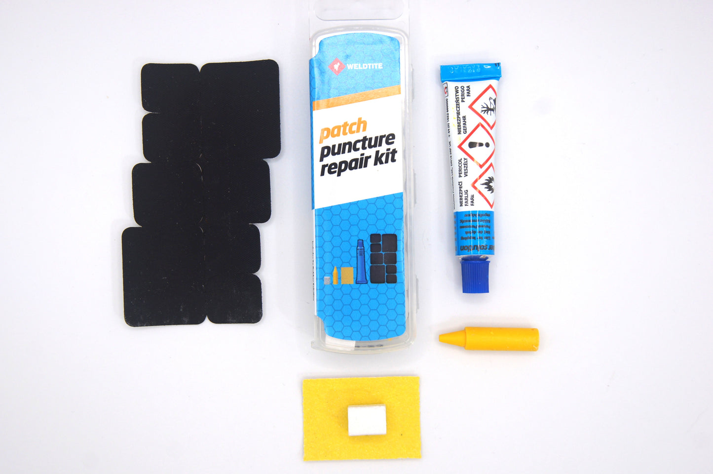 The image shows the contents of the Weldtite Patch puncture repair kit, including several black rubber patches, a tube of glue, sandpaper, a piece of chalk, and a blue package with instructions.